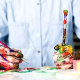 Paint-covered hands holding paintbrushes.