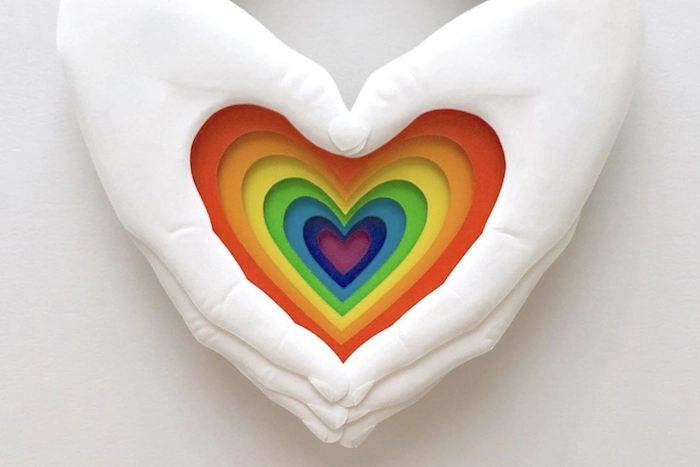 Pride artwork of two hands enclosing a rainbow-colored heart.