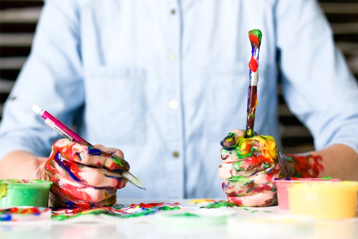 Paint-covered hands holding paintbrushes.